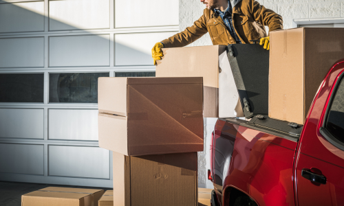 A farmer stacking cardboard boxes in the back of a pickup truck.